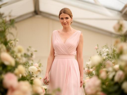 Wedding guest in a pastel occasion dress standing beside floral arrangements at a reception marquee